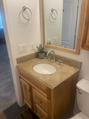 Un baño con lavamanos de encimera de granito, tocador de madera, espejo y retrete.