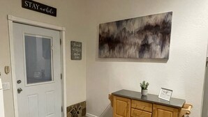 Un área de recepción con una puerta blanca, un muro de acento de piedra, un mueble de madera con cajones, una planta en maceta y un letrero que dice "STAY awhile".