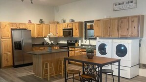 Cocina moderna con armarios de madera, electrodomésticos de acero inoxidable, una isla central con taburetes y un letrero que indica lavandería.