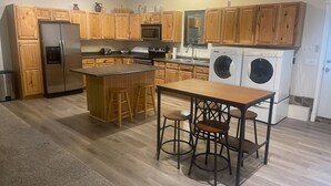 Una cocina con armarios de madera, un refrigerador de acero inoxidable, un microondas, un fregadero, una estufa y un taburete de bar.