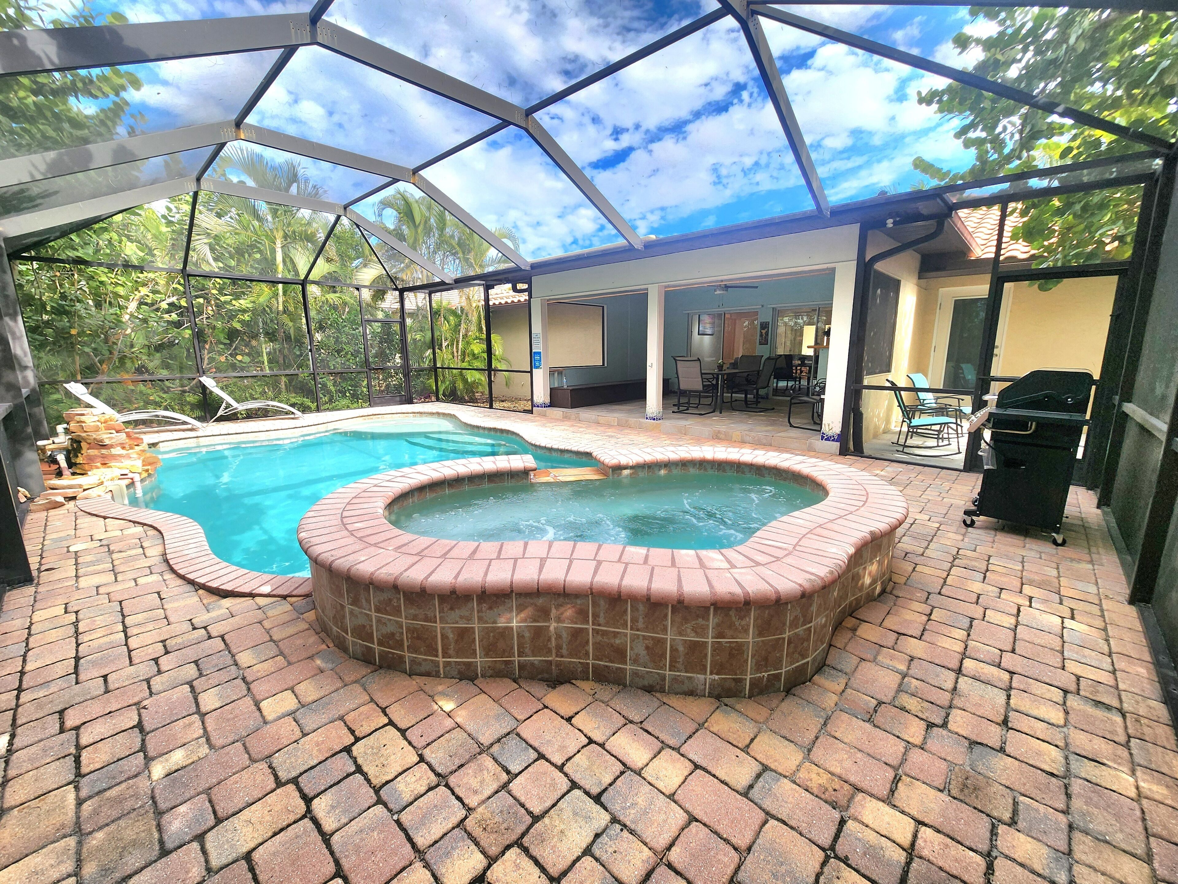Piscina ao ar livre coberta com hidromassagem, rodeada por um terraço de tijolos e um compartimento de vidro.