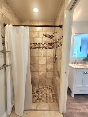 Un espace douche avec un sol carrelé, une pomme de douche et un rideau.