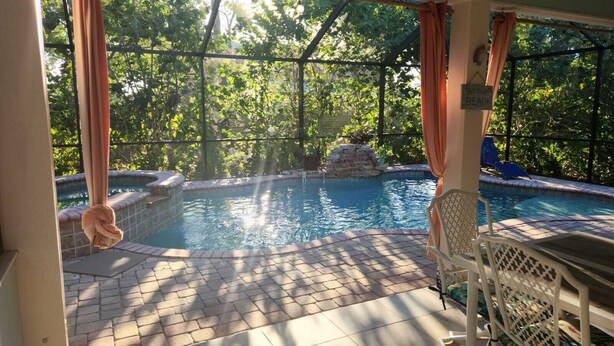 An outdoor pool area with a hot tub, surrounded by a covered patio with chairs and a table. - BEACH GETAWAY- 9 MIN FROM THE BEACH (Bonita Springs)