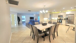 A modern kitchen with stainless steel appliances, a dining area with a marble table and chairs, and a visible TV in the background. - BEACH GETAWAY- 9 MIN FROM THE BEACH (Bonita Springs)