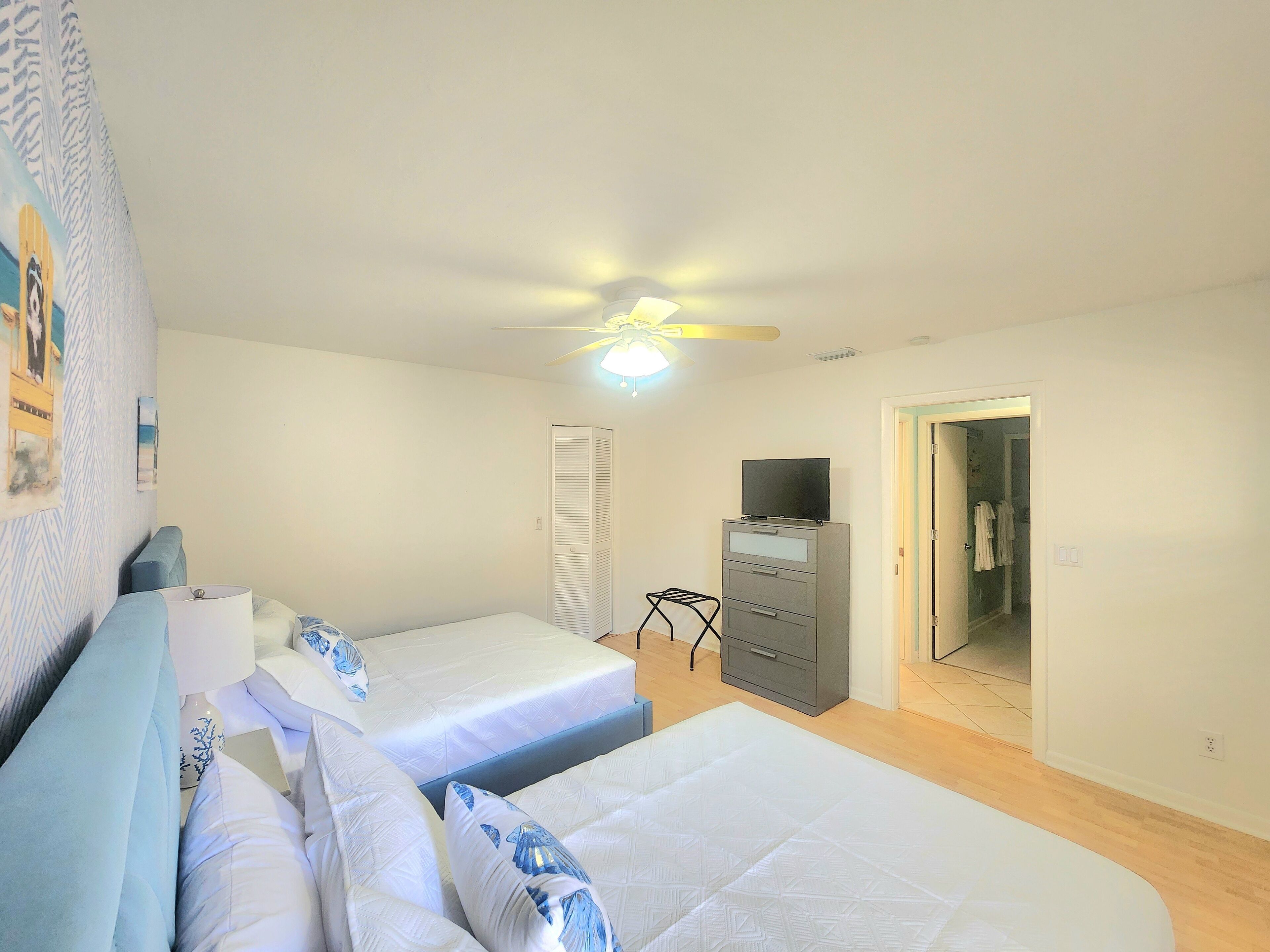 A bedroom with two beds, a ceiling fan, a dresser, and a door leading to another room.