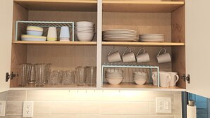 A kitchen with wooden cabinets, a granite countertop, and a hanging rack for cups and bowls. - BEACH GETAWAY- 9 MIN FROM THE BEACH (Bonita Springs)