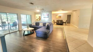 A spacious living area with a sectional sofa, a dining table with chairs, and a sliding glass door leading to an outdoor patio. - BEACH GETAWAY- 9 MIN FROM THE BEACH (Bonita Springs)