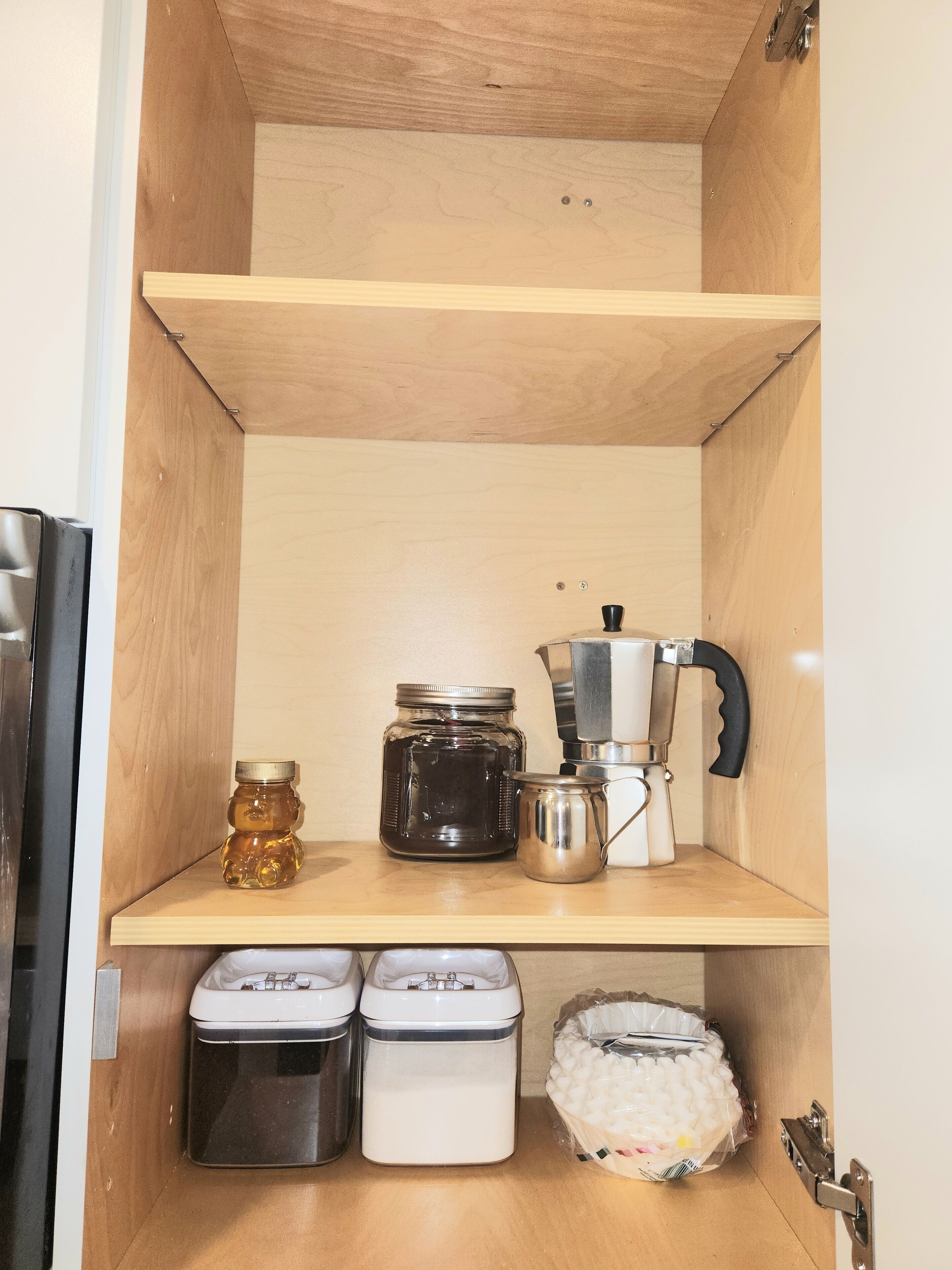 A wooden cabinet with shelves containing jars, a coffee maker, and containers.