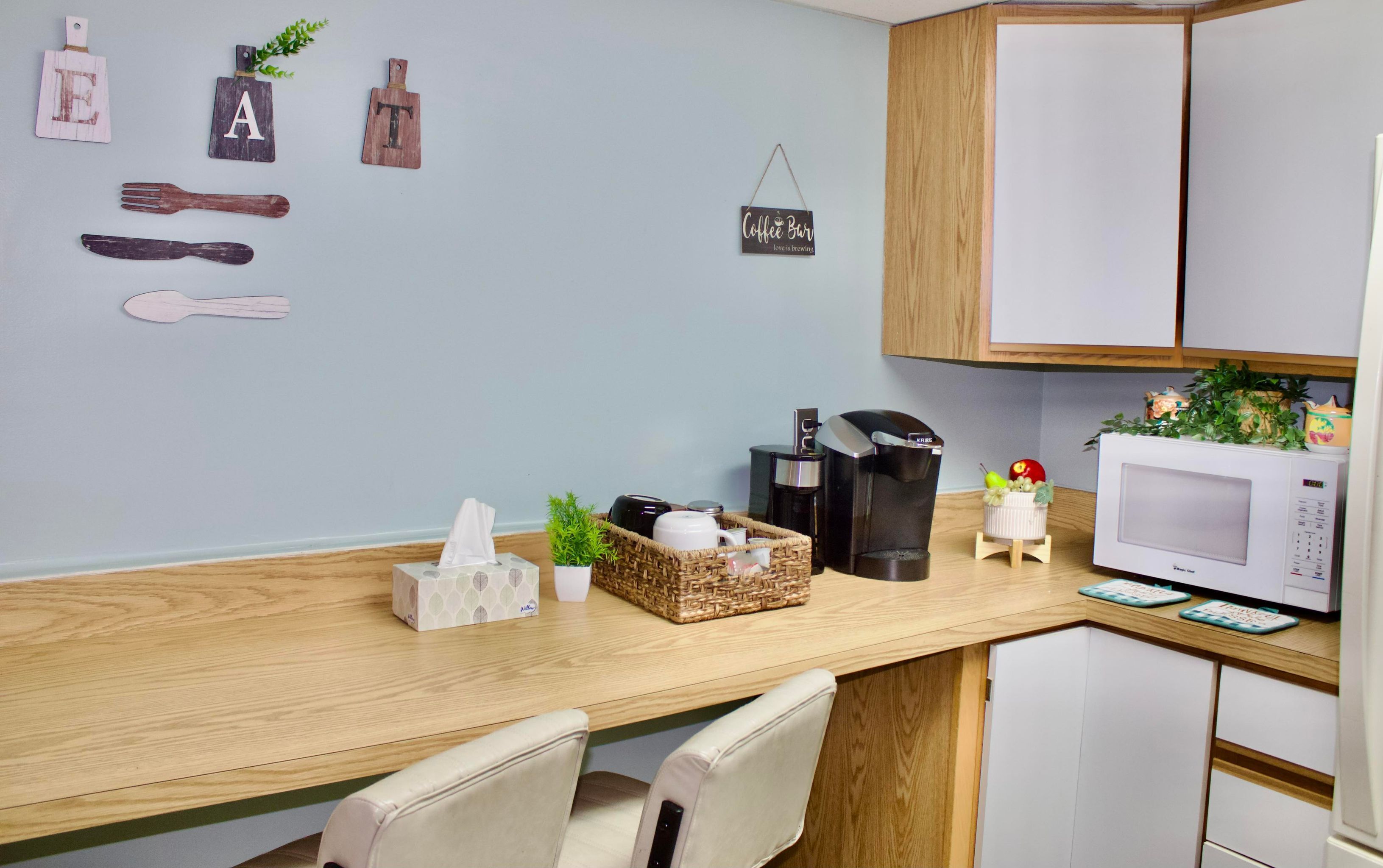 A kitchen with wooden cabinets, a microwave, a coffee maker, and a basket with kitchen items.