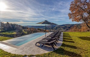 A swimming pool with lounge chairs and an umbrella, surrounded by a grassy area and a view of hills. - Awesome home in Boljun (Boljun)