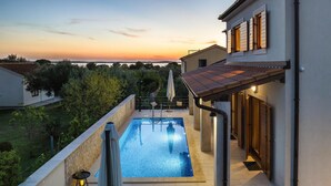 A swimming pool with a view of the sunset, a covered outdoor seating area, and a building with a tiled roof. - Awesome home in Peroj (Peroj)