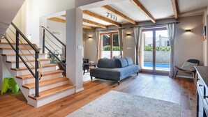A spacious living area with a wooden staircase, a grey sofa, and a view of a swimming pool through glass doors. - Awesome home in Peroj (Peroj)