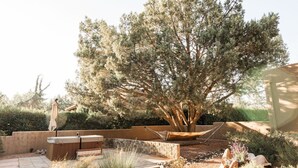 A patio area with a hot tub, a hammock, and a large tree.