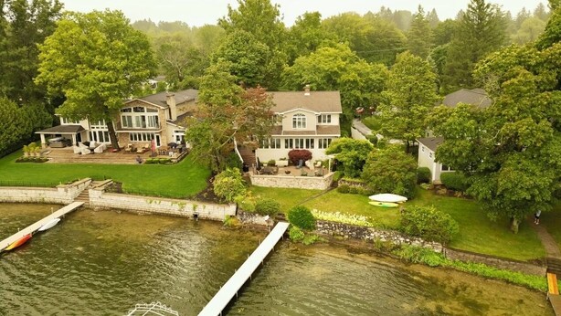 A large house with a dock extending into a lake, surrounded by lush greenery and trees.