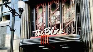 Un edificio con un letrero que dice "The Block" y un logotipo. Presenta una fachada moderna con patrones geométricos y una entrada negra con puertas de vidrio.