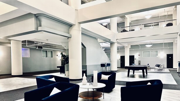 Un vestíbulo espacioso con techos altos, muebles modernos y una escalera central.