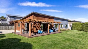 Une maison moderne dotée d’une terrasse en bois, d’un patio couvert et d’une pelouse bien entretenue.