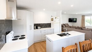 Une cuisine moderne avec des meubles blancs, un îlot central doté d’une cuisinière et un coin repas avec des chaises en bois.