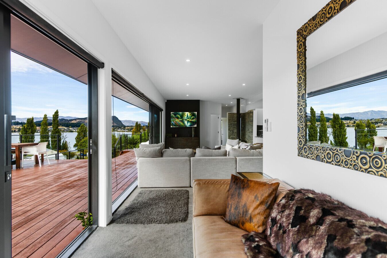 Una sala de estar moderna con un sofá grande, televisión y vistas a un lago y montañas.
