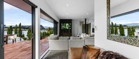 Una sala de estar moderna con un sofá grande, televisión y vistas a un lago y montañas.