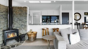 Una sala de estar moderna con chimenea de piedra, una cocina con baldosas azul oscuro y un sofá gris.
