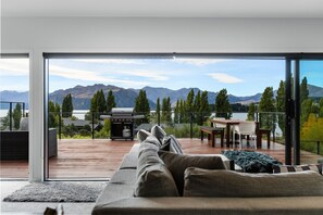 A modern living room with a large sofa, a dining area, and a grill outside. - The Lookout: Lake Views (Wanaka)