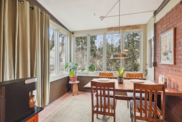 A dining area with a brick wall, wooden table, chairs, and potted plants.