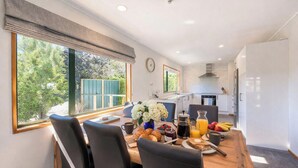 A modern kitchen with a dining area, large windows, and a view of greenery.
