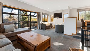 A spacious living area with a large window, a sofa, a coffee table, and a TV mounted on the wall.