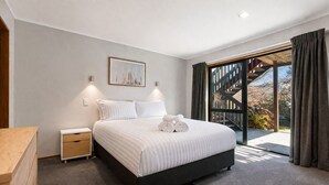 A bedroom with a bed, bedside tables, a nightstand, a framed picture on the wall, and a view through a glass door.