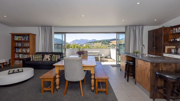 Un espace de vie moderne comprenant un coin repas, une cuisine et une grande porte-fenêtre coulissante donnant sur un balcon avec vue sur la montagne.
