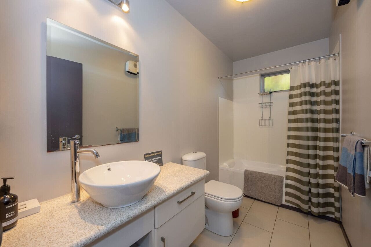 A modern bathroom with a large mirror, a white sink, a toilet, and a shower area.