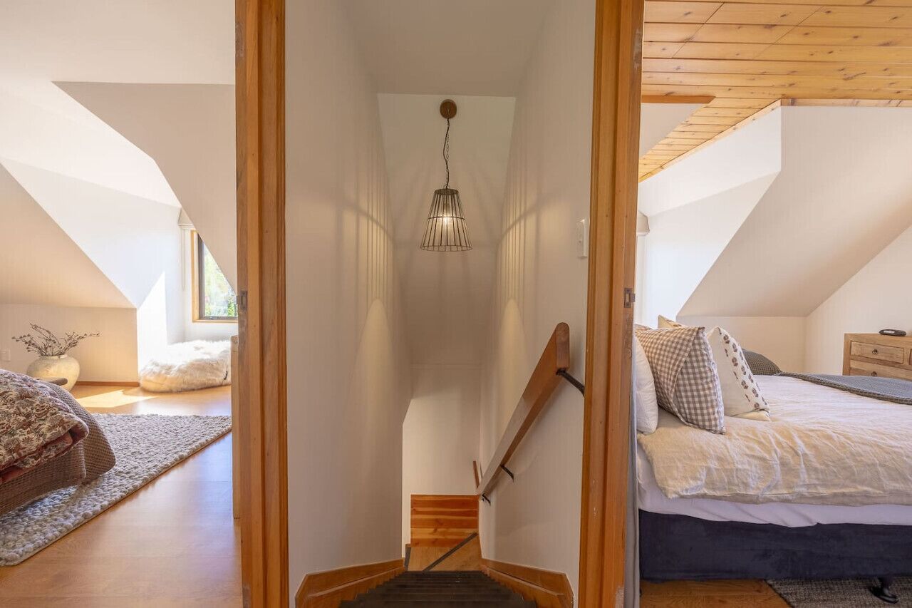 A bedroom with a wooden staircase, a bed with pillows, and a hanging light fixture.