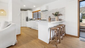 Une cuisine moderne avec des meubles blancs, un îlot central doté de tabourets de bar et une fenêtre avec des stores.