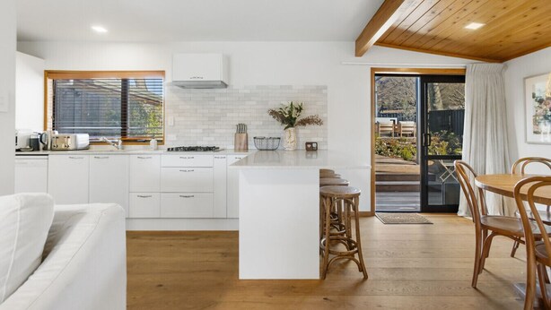 Une cuisine moderne avec des meubles blancs, un îlot central et un coin repas doté de chaises en bois.