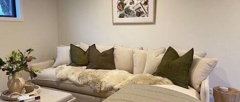 A modern living room with a sofa, ottoman, and a painting on the wall.