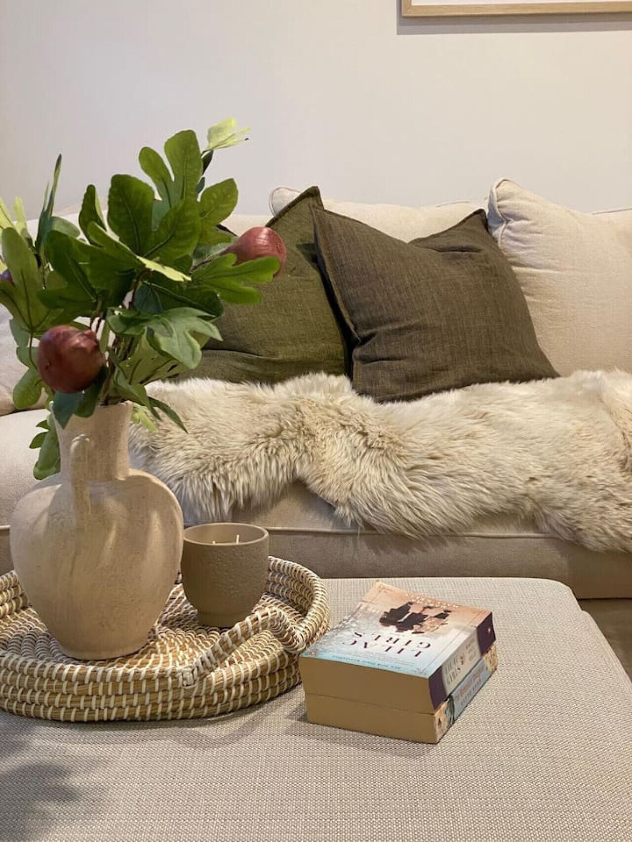 Ein gemütliches Wohnzimmer mit einer Couch, einer flauschigen Decke, einer Vase mit Pflanze, einer Kerze und einer Büchersammlung.