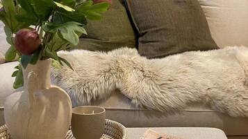 Ein gemütliches Wohnzimmer mit einer Couch, einer flauschigen Decke, einer Vase mit Pflanze, einer Kerze und einer Büchersammlung.