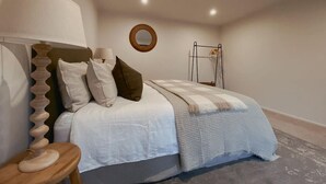 A bedroom with a bed, pillows, a lamp, a circular mirror, and a wooden ladder against the wall. - Wanaka Deluxe Studio (Wānaka)