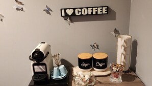 Decoración con tema de café, que incluye vinilos decorativos en la pared, una cafetera, recipientes para azúcar y café, y un mueble de almacenamiento de madera.