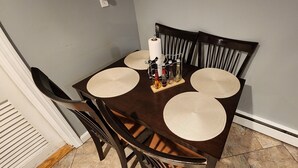 Una mesa de comedor con cuatro individuales tejidos, un rollo de servilletas de papel y varias botellas sobre una bandeja.
