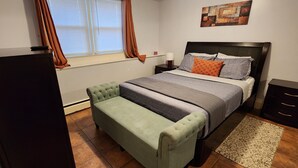 Un dormitorio con cama, mesita de noche, cómoda, televisor, ventana con cortinas y una pequeña mesa.