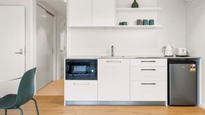 A modern kitchen with white cabinetry, a built-in microwave, a coffee machine, and a refrigerator. - Studio Guest Home with Roys Peak Views (Wānaka)