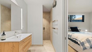A modern bedroom with a bed, a window, and a bathroom with a mirror and sink. - Studio Guest Home with Roys Peak Views (Wānaka)
