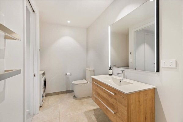 Une salle de bain moderne avec un lavabo blanc, un meuble-lavabo en bois et un grand miroir.