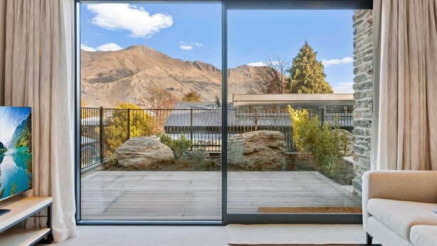 A modern living room with a large sliding glass door leading to a balcony with a mountain view. - Studio Guest Home with Roys Peak Views (Wānaka)