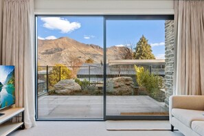 Un salon moderne doté d’une grande porte-fenêtre coulissante donnant sur un balcon avec vue sur les montagnes.