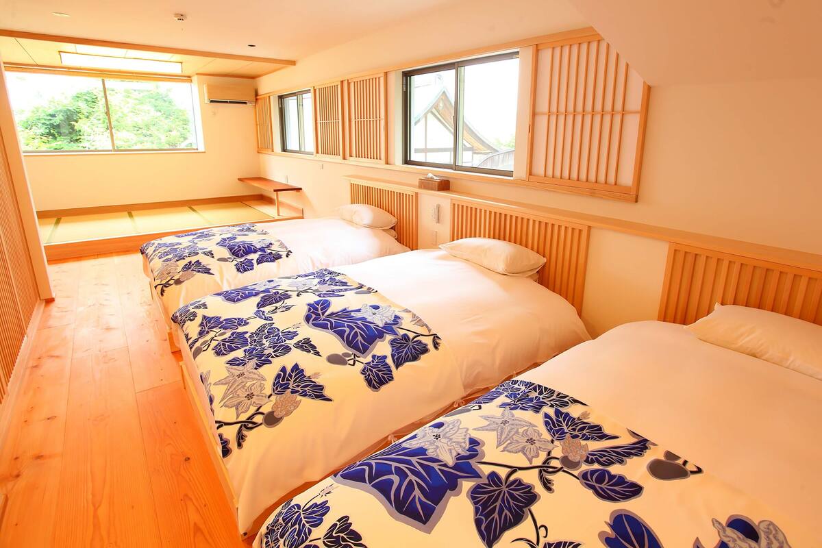 Une chambre avec trois lits, un plancher en bois et de grandes fenêtres.