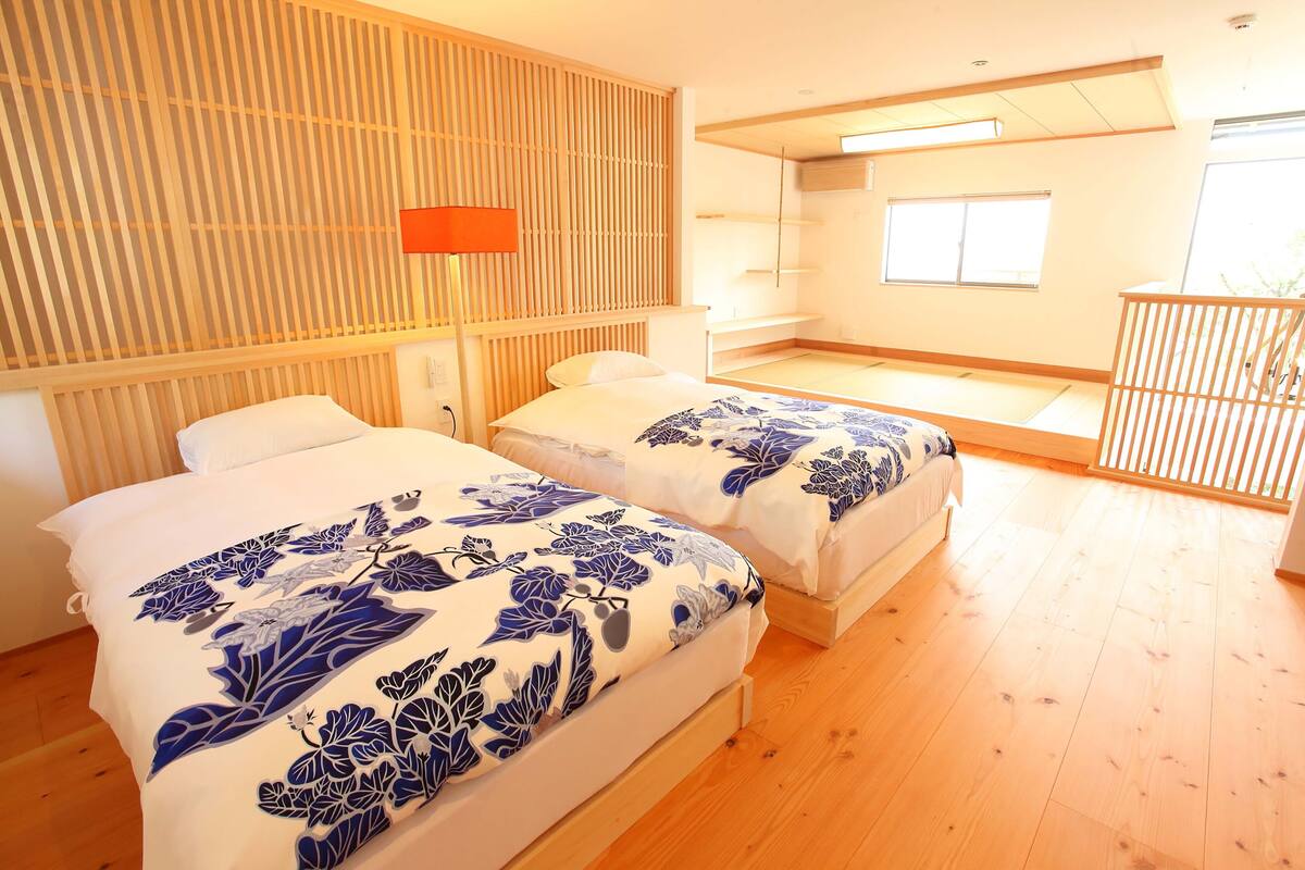Une chambre d’hôtel avec deux lits, un mur en lambris de bois, une fenêtre et un balcon.