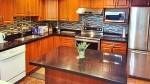 A modern kitchen with wooden cabinets, a stainless steel refrigerator, a microwave, and a central island with a vase of flowers. - Chinese style suite near golf course (Surrey)